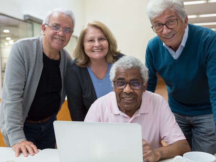 Older friends smiling in front of a laptop